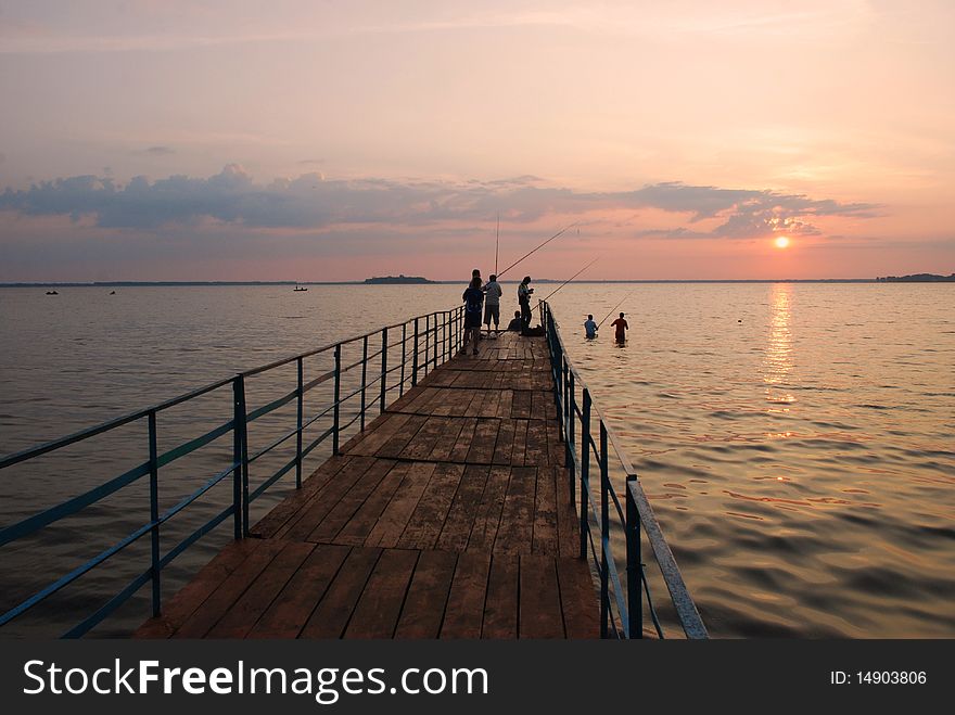 Sunrise on lake with a pier and fishermen. Sunrise on lake with a pier and fishermen.