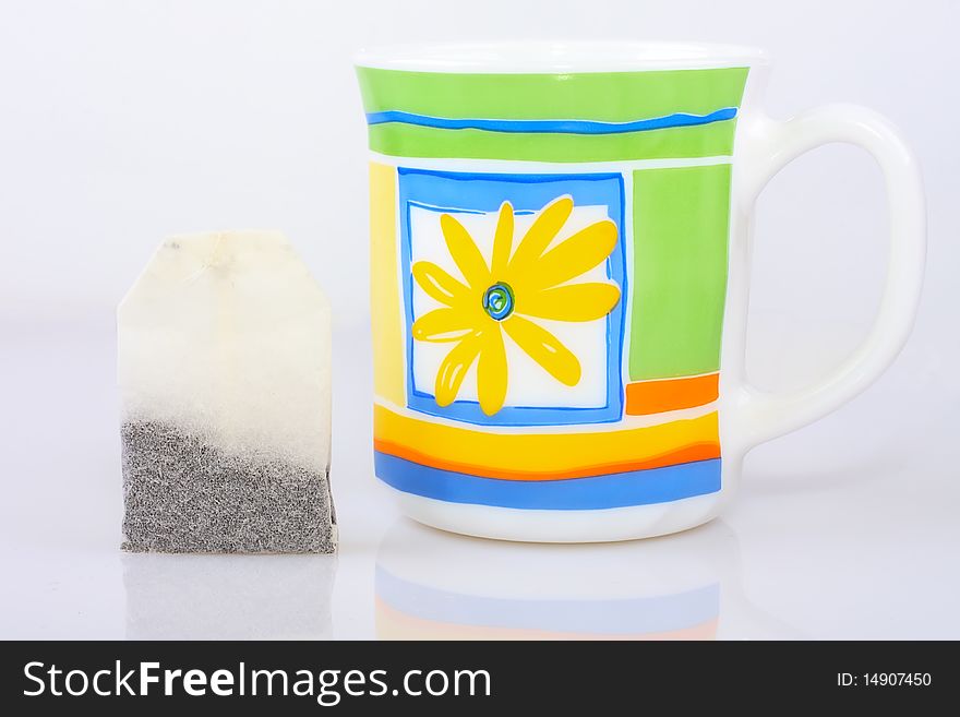 Mug with yellow flowers and standing next to a tea bag. Mug with yellow flowers and standing next to a tea bag