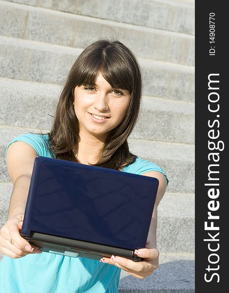 Woman outdoors sitting on the steps the school with a laptop. Notebook in hand stretched out in the frame. Woman outdoors sitting on the steps the school with a laptop. Notebook in hand stretched out in the frame