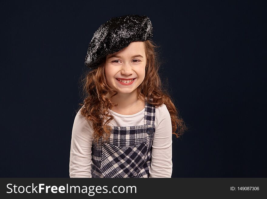 Stylish brunette kid is posing in studio on a black background. Children`s fashion.