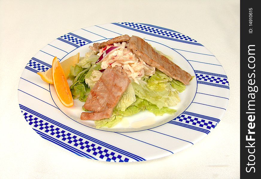 The hot appetizer with pieces of tuna on the round white plate with blue ornament. The dish is decorated with slices of citrus. The hot appetizer with pieces of tuna on the round white plate with blue ornament. The dish is decorated with slices of citrus.