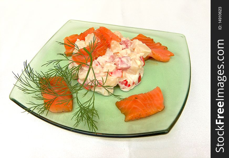 In the center of the green glass plates placed salad of boiled potatoes, soy sauce, tomato, egg, mayonnaise. The edges of the plates are pieces of salmon. The dish is decorated with a sprig of dill.