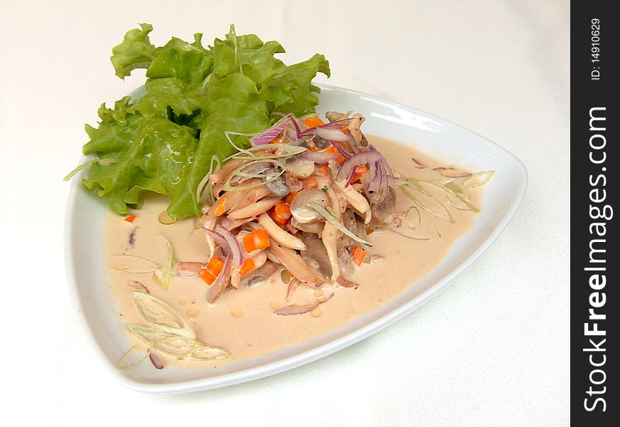 Pieces of squid with creamy sauce with vegetables and mushrooms on a leaf of lettuce in a white triangular ceramic plate. Pieces of squid with creamy sauce with vegetables and mushrooms on a leaf of lettuce in a white triangular ceramic plate.