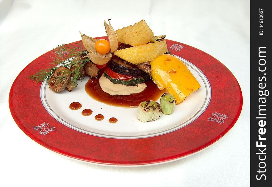 The pork chop with grilled vegetables and champignons under two sauses on the white plate with red border. This dish is decorate a winter cherry and dill. The pork chop with grilled vegetables and champignons under two sauses on the white plate with red border. This dish is decorate a winter cherry and dill.