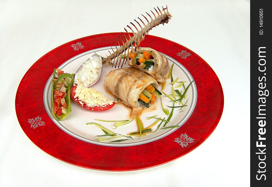 Fillet of seabass simmered with vegetables on the red plate with red border. This fish dish is decorate a fishbone. Fillet of seabass simmered with vegetables on the red plate with red border. This fish dish is decorate a fishbone.