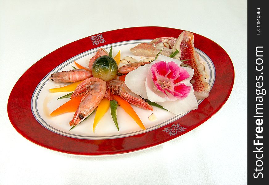 The fillet of red mullet an almond sauce, shrimps and pieces of vegetable on the oval plate with red border. The fillet of red mullet an almond sauce, shrimps and pieces of vegetable on the oval plate with red border.