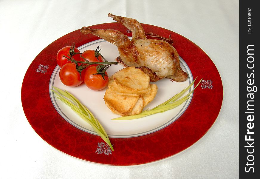 The quail braised carbonado, cherry tomatoes, potato chips and pieces of greenery  on the round plate with red border. The quail braised carbonado, cherry tomatoes, potato chips and pieces of greenery  on the round plate with red border.