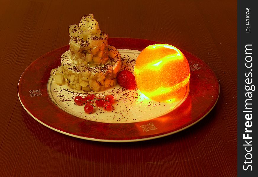 The red plate of fruit dessert. This fruit dessert is collected in three-storey a pyramid and decorated with wood berry. The cut peel of an orange is collected in the whole, inside it burns small candle. The red plate of fruit dessert. This fruit dessert is collected in three-storey a pyramid and decorated with wood berry. The cut peel of an orange is collected in the whole, inside it burns small candle.