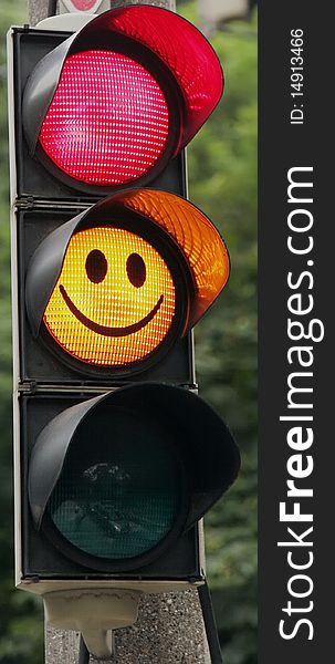 Traffic signal, on which lights the red one and the yellow one. There is a grinning face in the yellow one symbol. Focus on the lighting lamps. Traffic signal, on which lights the red one and the yellow one. There is a grinning face in the yellow one symbol. Focus on the lighting lamps.