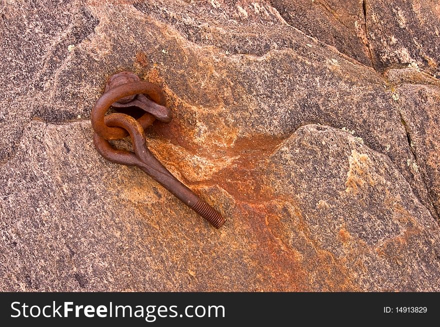 Rusty metal anchor on a rock covered with red iron oxide.