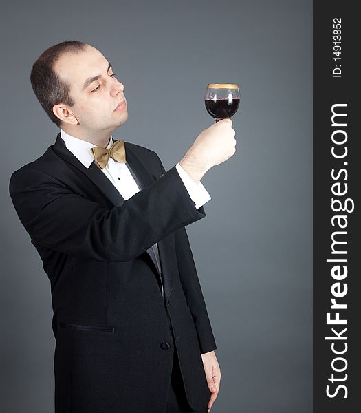 Man in tuxedo looking at the glass filled with red wine. Man in tuxedo looking at the glass filled with red wine.