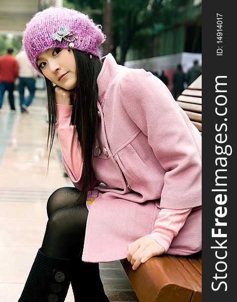 Beautiful girl sitting on bench in the street,smiling,in pink coat