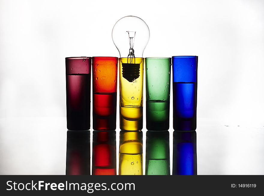 Colorful glasses with bulb on reflection table. Colorful glasses with bulb on reflection table