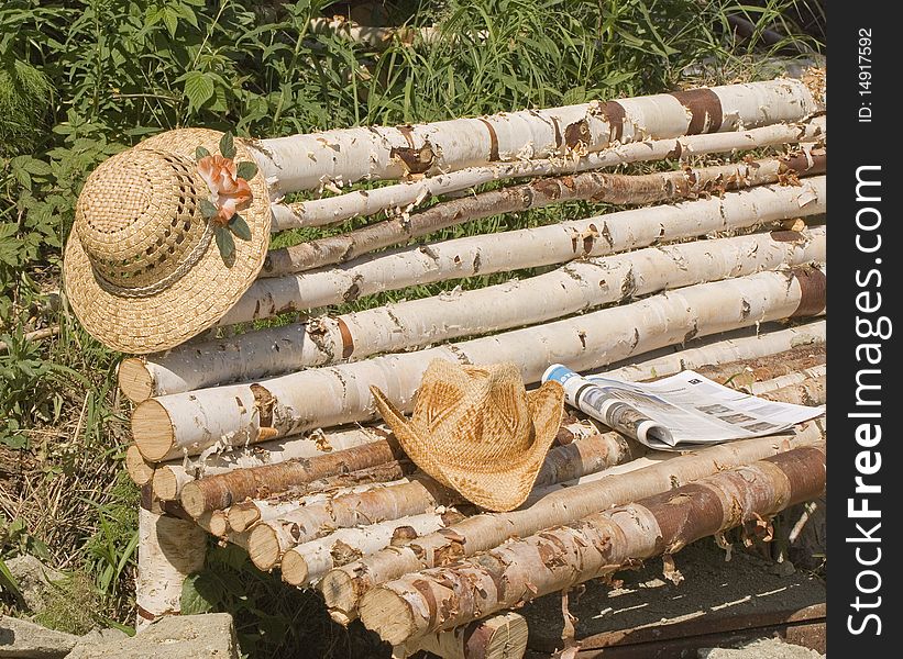 Straw hat with a pink flower on a branch of a pine on a birch bench in years to a garden. Straw hat with a pink flower on a branch of a pine on a birch bench in years to a garden