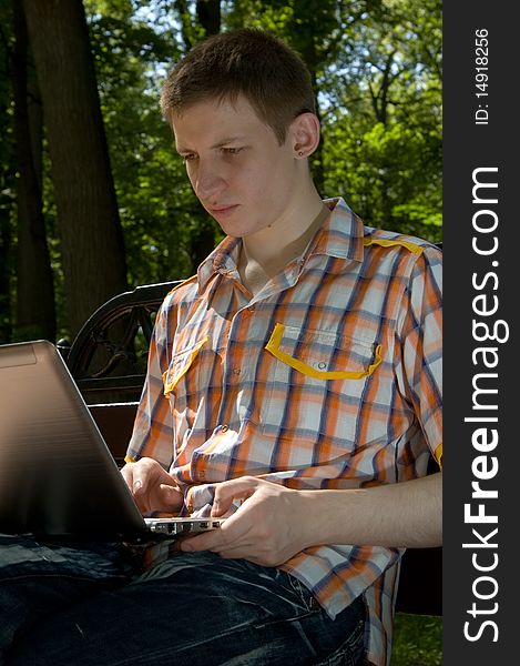 Young man sitting on a bench in green park and types on laptop. Young man sitting on a bench in green park and types on laptop