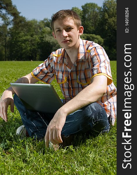 Young man sitting on green grass in park and types on laptop. Young man sitting on green grass in park and types on laptop