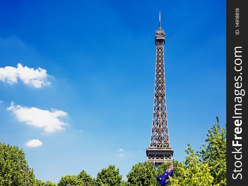 Eiffel Tower, with cloudy blue sky and sunny trees around.