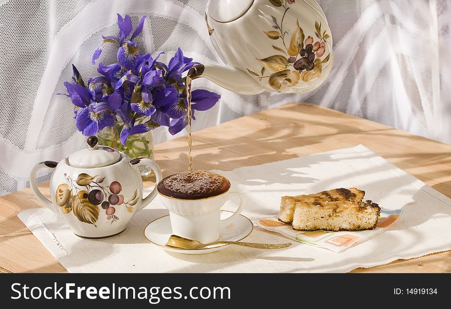 White cup from thin porcelain with a gold strip and the 
gold spoon on a background of dark blue colors of an 
iris. White cup from thin porcelain with a gold strip and the 
gold spoon on a background of dark blue colors of an 
iris