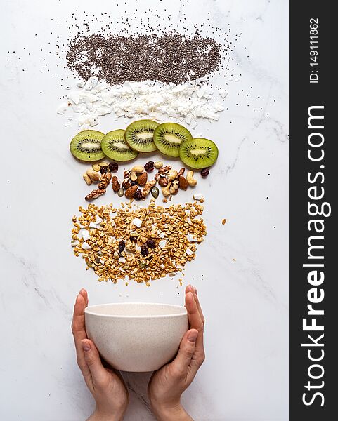 Healthy breakfast concept, female hand holding bowl with granola nuts kiwi chia seeds on white background, morning organic food with diet on table, detox meal for health nutrition vertical top view