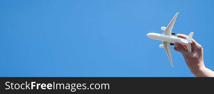 Hand holding airplane model in front of blue sky background. Travel