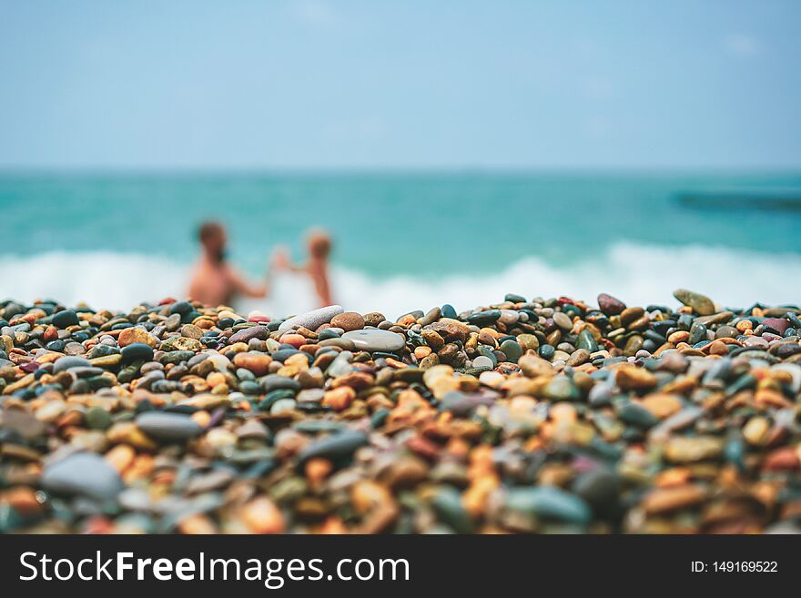 Father and baby son playing in water, blurred with pebbles in the foreground