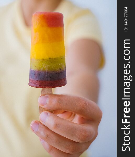 Girl with a yellow t-shirt holding a rainbow popsicle in her hands. Girl with a yellow t-shirt holding a rainbow popsicle in her hands