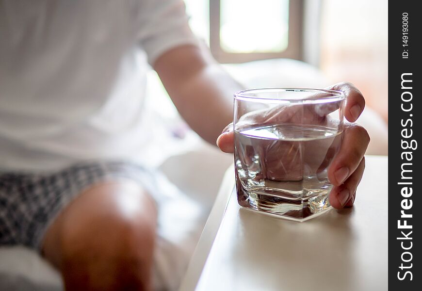 Hand of man holding a clear glass of water for drinking on bed in the Morning.