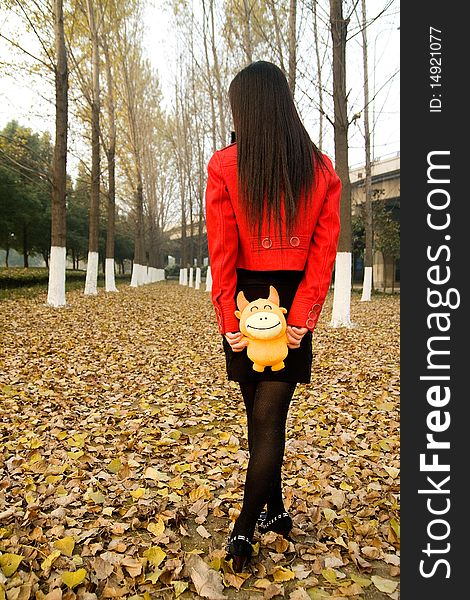 Beautiful girl walking on defoliation,in red coat,puppet in hands