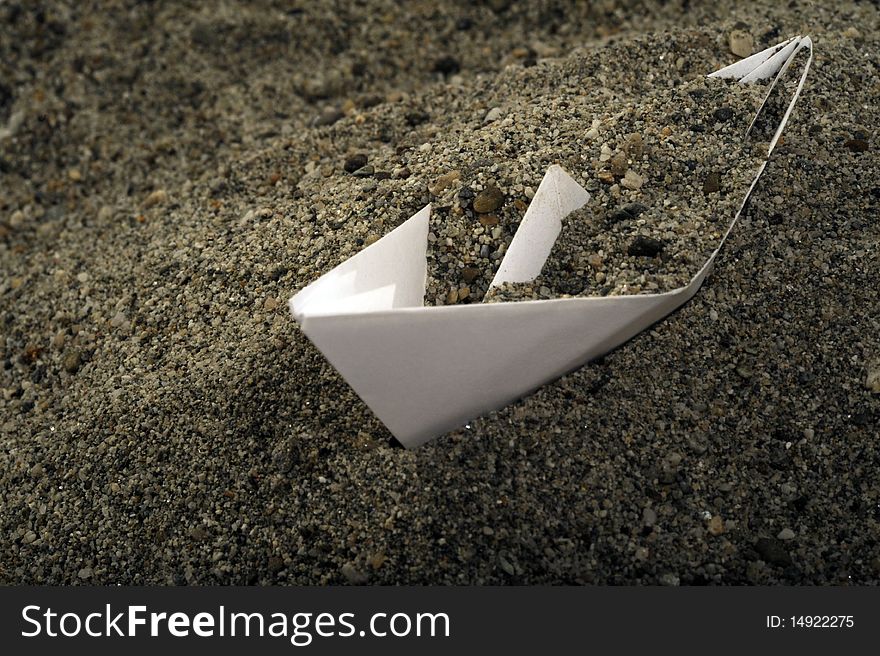 A toy white paperboat under a lot of sand. A toy white paperboat under a lot of sand.