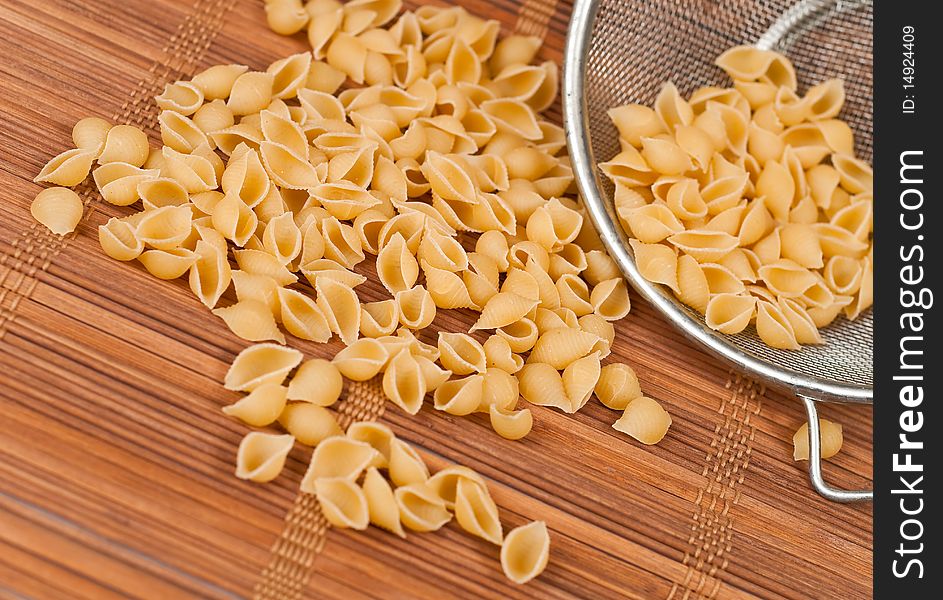 Dry shell pasta on bamboo mat with strainer. Dry shell pasta on bamboo mat with strainer