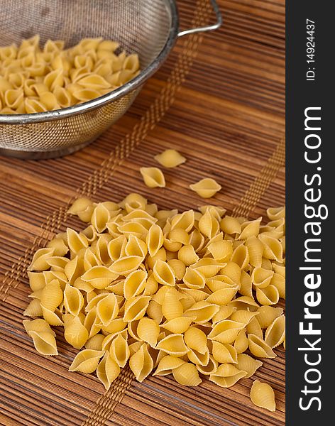 Dry shell pasta spilled out of a strainer. Dry shell pasta spilled out of a strainer