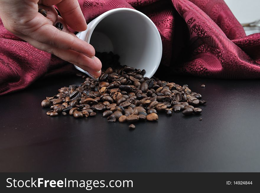 Coffee granules on black table with cup and hand with red velvet scarf