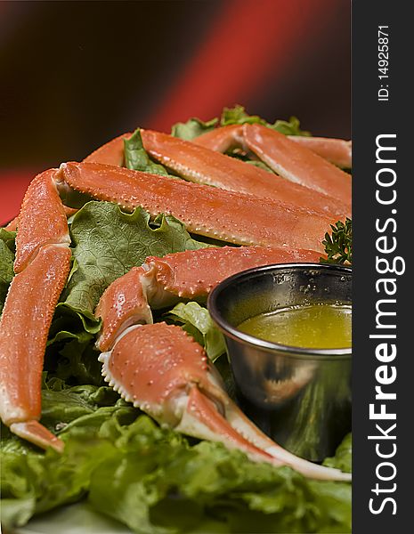 A red crab pinch and legs near some melted butter on a salad sheet.