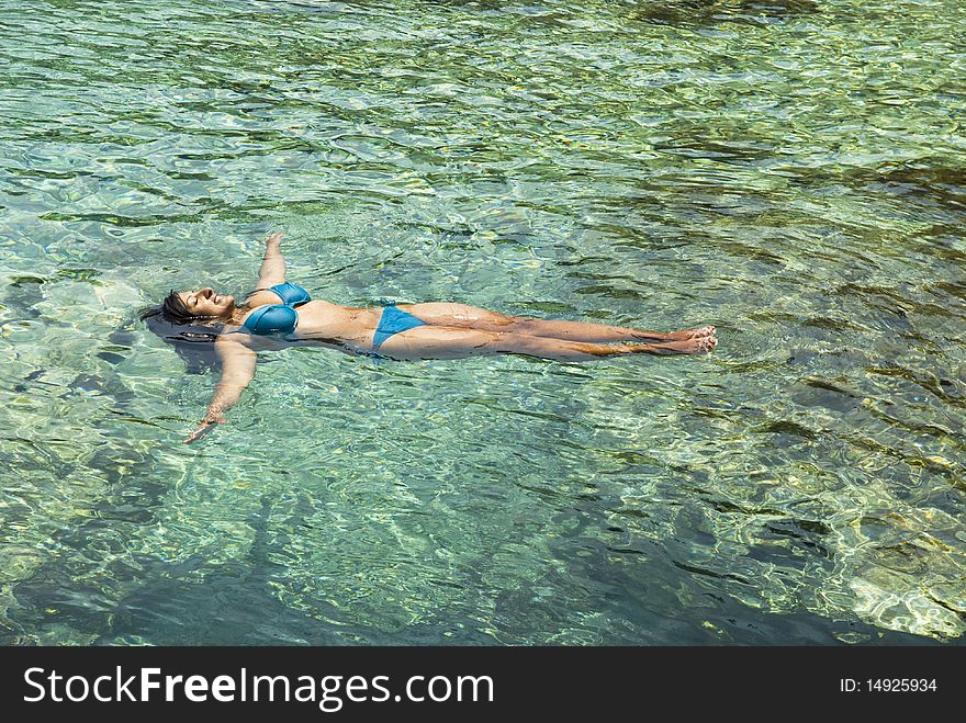 A color photo of a beautiful indian woman relaxing as she floats in the clear blue colored sea while wearing a bikini during her summer vacation. A color photo of a beautiful indian woman relaxing as she floats in the clear blue colored sea while wearing a bikini during her summer vacation.