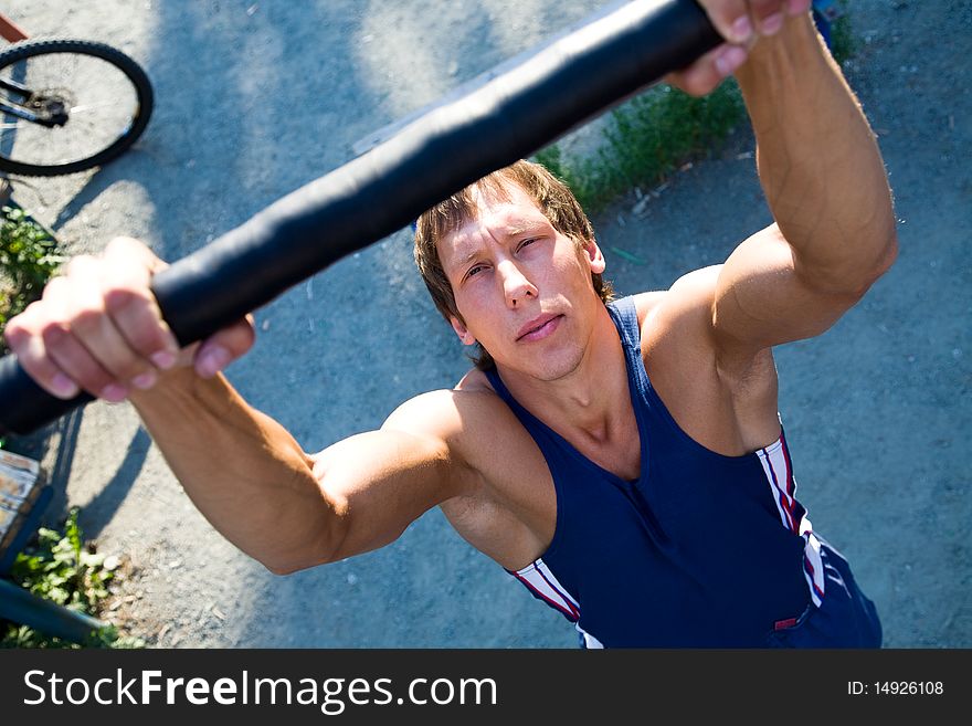 Young handsome man performs sport exercises to strengthen muscles outdoors. Young handsome man performs sport exercises to strengthen muscles outdoors