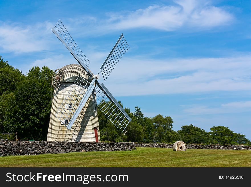 Historic New England windmill behind a stone fence and in a grassy field. Historic New England windmill behind a stone fence and in a grassy field