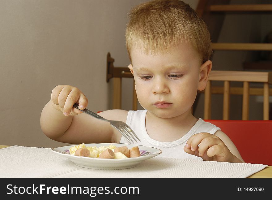 Small cute boy eats his dinner himself. Small cute boy eats his dinner himself