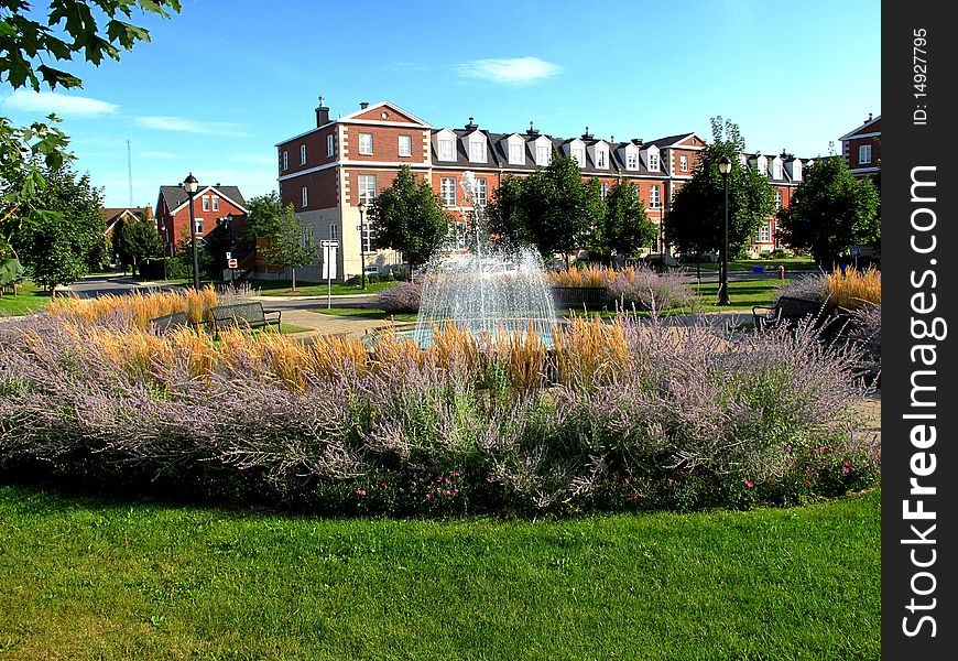 A fountain in a gardin surrounded by town homes.
