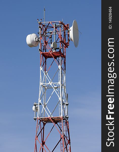 Red and white tower of communications with with a lot of different antennas under clear sky.