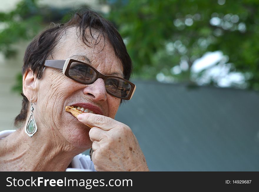 An old lady is using her new teeth to bite something delicious. An old lady is using her new teeth to bite something delicious