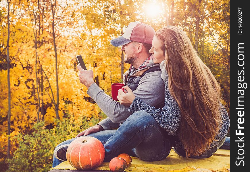 Handsome men and stylish women holding a mobile phone and sitting on the terrace against the background of yellow trees and the setting sun. Happy relationship concept. Handsome men and stylish women holding a mobile phone and sitting on the terrace against the background of yellow trees and the setting sun. Happy relationship concept