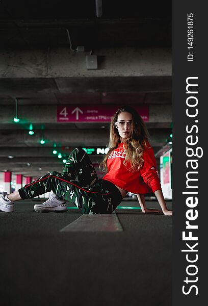 Pretty young woman sitting on car parking. Wearing stylish urban outfit