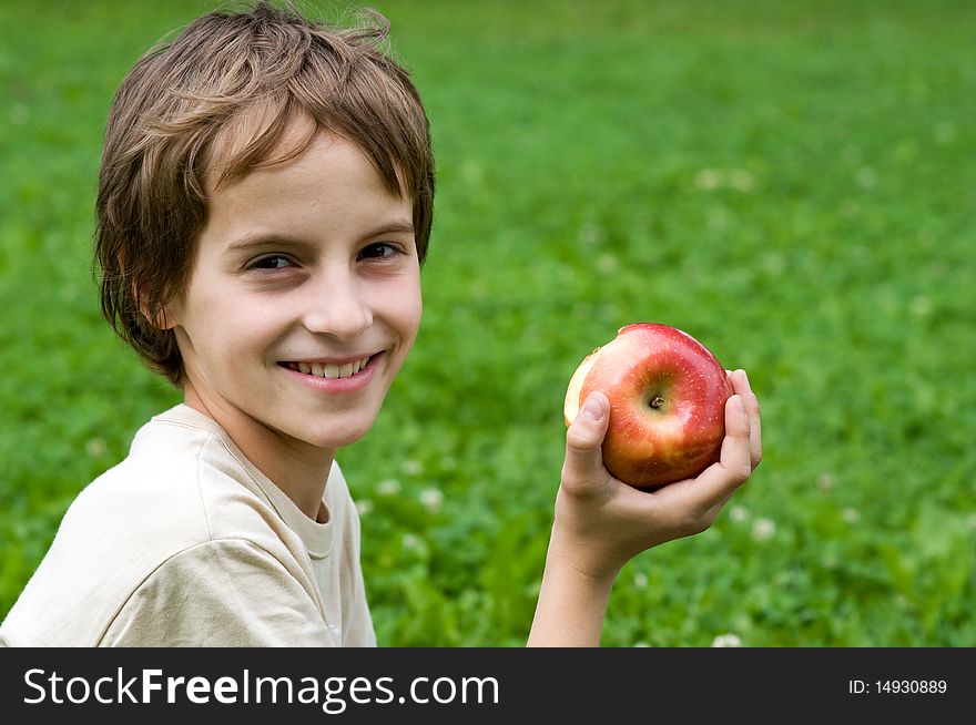 Portrait of a preteen boy with a apple in his hand and green grass in the background. Portrait of a preteen boy with a apple in his hand and green grass in the background