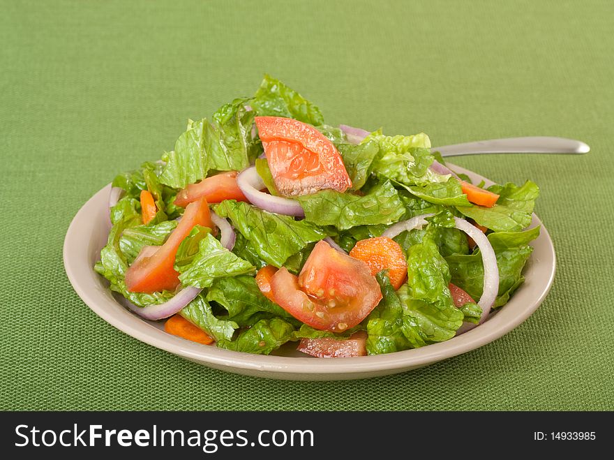 Tossed salad with lettuce, tomatoes, onions and carrots on a green table cloth