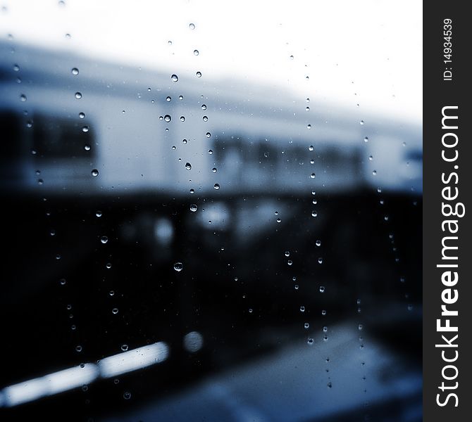 Rain drops on the window on a rainy day. The Building in the backdrop is a local railway station in Tokyo. Rain drops on the window on a rainy day. The Building in the backdrop is a local railway station in Tokyo.