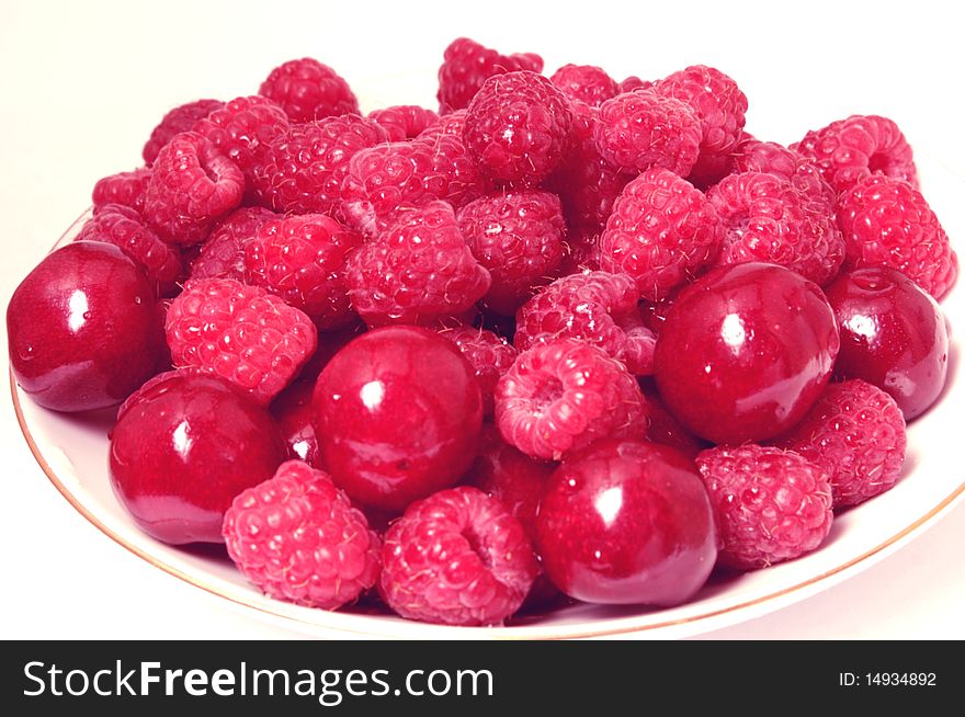 On farforofom saucer many raspberries and cherries, ripe red berries on a white background. On farforofom saucer many raspberries and cherries, ripe red berries on a white background