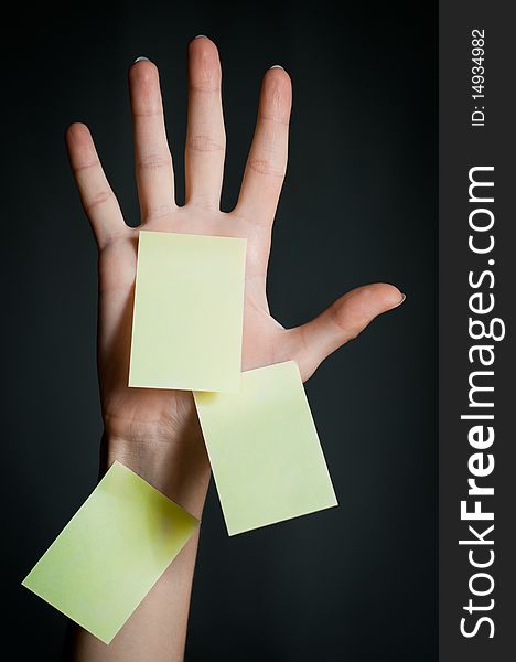 Female hand with three office sticky notes on dark background . All notes are blank and yellow. Female hand with three office sticky notes on dark background . All notes are blank and yellow