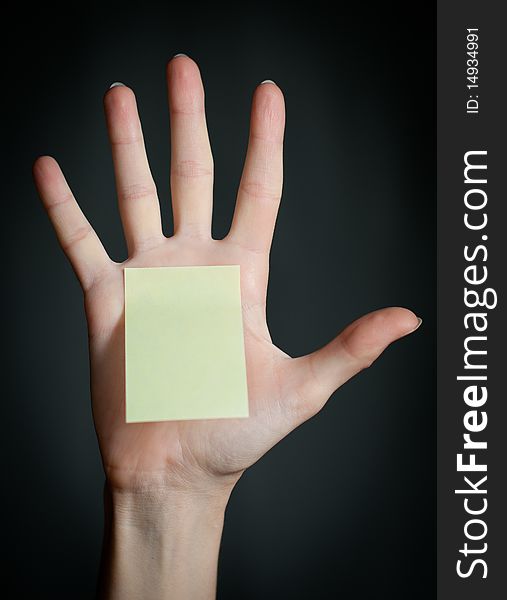 Female hand with sticky office note on dark background . Note is blank and yellow. Female hand with sticky office note on dark background . Note is blank and yellow