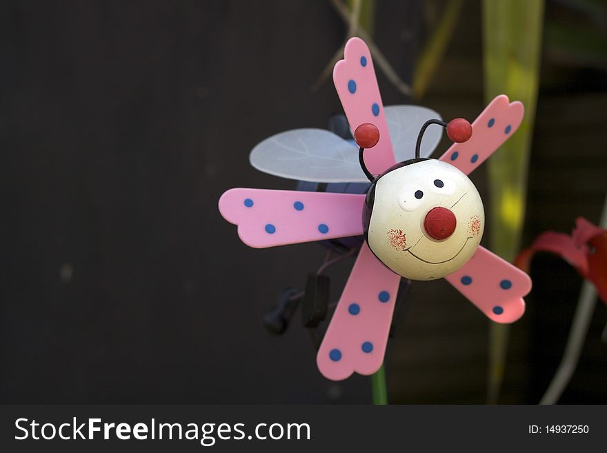 A child's plastic plant pot toy decoration of a stylised bee with pink wings. Set in a garden flower pot. A child's plastic plant pot toy decoration of a stylised bee with pink wings. Set in a garden flower pot.