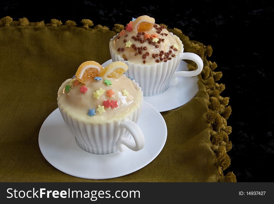Decorated cupcakes in white teacup molds against a black background. Decorated cupcakes in white teacup molds against a black background
